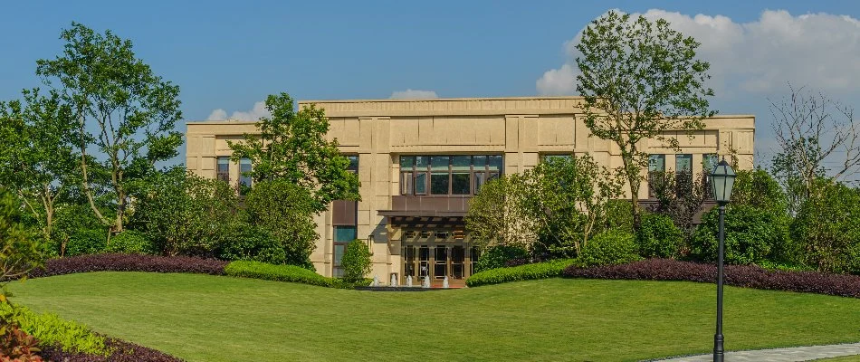 Building in Milan, MI, behind a green lawn and tall trees.